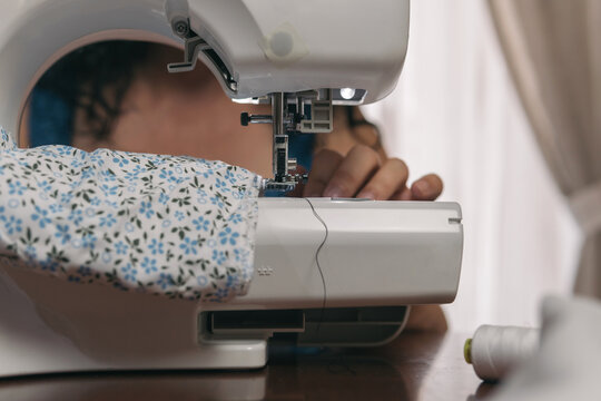 Close-up image of an automatic sewing machine. Unrecognizable woman's hands trying to spin a piece of fabric on her tool.
