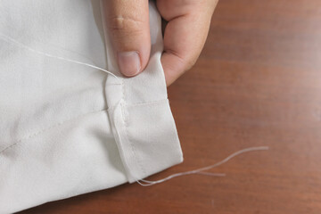 Close-up of unrecognizable woman's hands sewing with white thread her pants to fix them. Woman seamstress doing home tailor work.