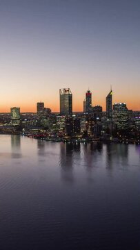 Illuminated cityscape view with high and modern skyscrapers with a lake water at sunset in Perth
