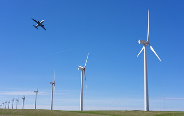 Airplane flying over a wind turbine farm.  Renewable wind energy against the blue sky.