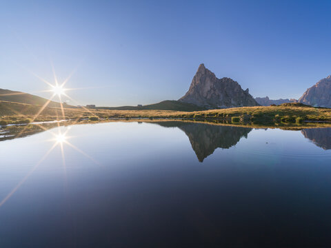 Ra Gusela mountain at Passo Giau and the sun starbeam perfectly reflected in an alpine lake, Dolomites, Italy