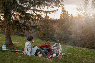 Caucasian young friends sitting at fire in mountains, playing on guitar and singing. Tourism. 
