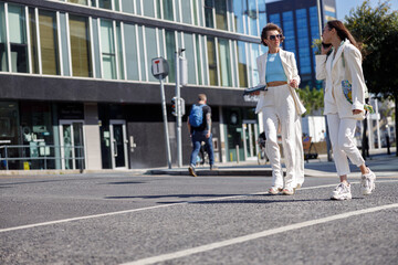 Two happy woman in trendy outfits laugh and walk outside on background of modern building