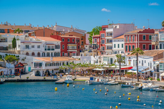 View of colourful cafes, restaurants and boats in harbour against blue sky, Cales Fonts, Menorca, Balearic Islands, Spain
