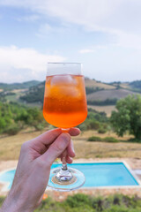 Hand holding an aperitif spritz cocktail with a beautiful italian view behind