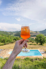 Hand holding an aperitif spritz cocktail with a beautiful italian view behind