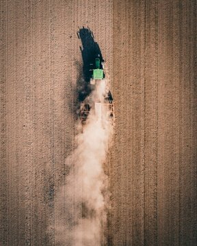 Vertical drone shot of a tractor working in the field and making dust