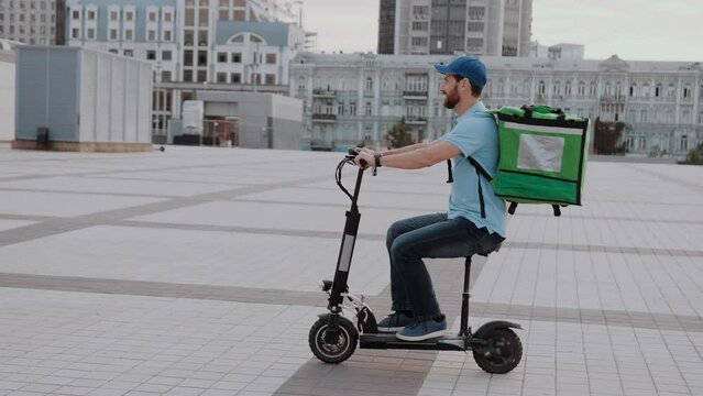 Man courier food delivery with thermal backpack rides the street on an electric scooter deliver online order client customer. Deliveryman worker employee