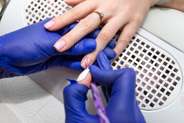 The manicurist paints her nails with pink hybrid varnish, and with a thin brush she paints pink dots.