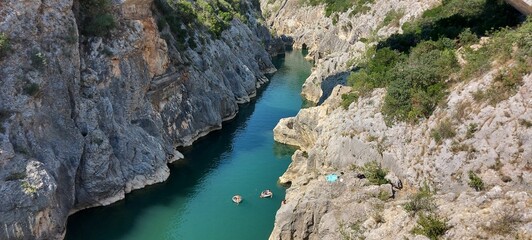 Aerial view of a blue river flowing in a rural area surrounded by rocky cliffs on a sunny day