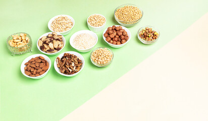 Lot of cereals and nuts in bowls on beige-green backdrop. View from side above. Copy space.