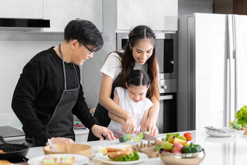 Obraz na płótnie Canvas Asian girl learning to cook with mom and dad. Do activities together with your family in a fun and joyful way. There is a father and mother taking care of them closely.