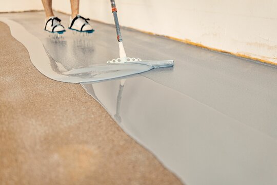 Construction worker apply grey epoxy resin in an industrial hall