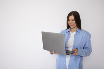 Smiling woman with white teeth in a blue shirt and a white t-shirt holds a laptop on a white background isolate. Concept: female freelancer. Woman in casual clothes. Mockup place for text. banner