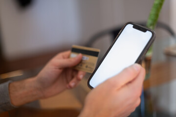 Close up young man holding bank credit card and modern tech device with mock up white screen in hands, enjoying purchasing goods in internet store using mobile phone application, online shopping
