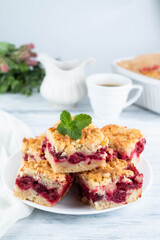 Blurred image of cherry pie slices in a plate, a cup of coffee, a jug of milk, a pie in shape on a light table.