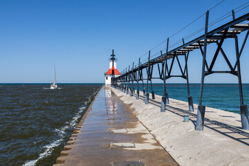 Obraz premium Sailboat going out the channel at St. Joseph North Pier Lighthouse, Michigan