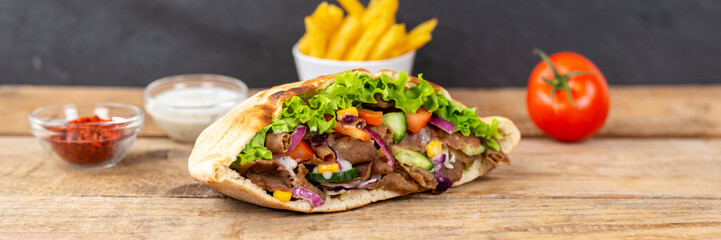 Döner Kebab Doner Kebap fast food meal in flatbread with fries on a wooden board panorama