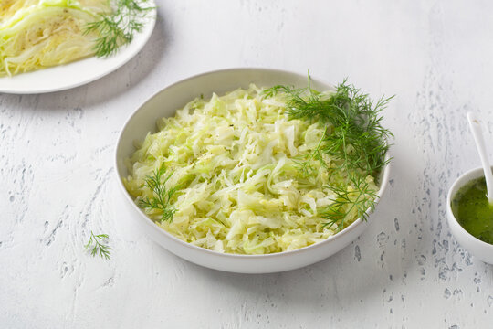 Steam white cabbage in a white ceramic bowl with herbs and green sauce on a light blue background, top view. Delicious diet food