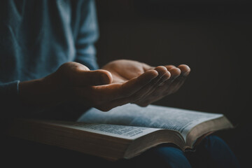 Hands open palm up in prayer on a Holy Bible in church concept for faith, spirituality, and...