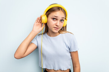 Young caucasian girl listening to music isolated on blue background trying to listening a gossip.