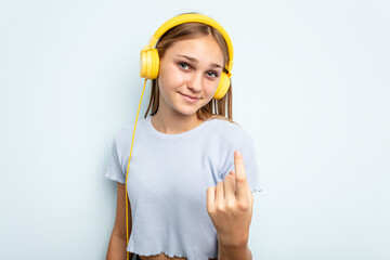 Young caucasian girl listening to music isolated on blue background pointing with finger at you as if inviting come closer.