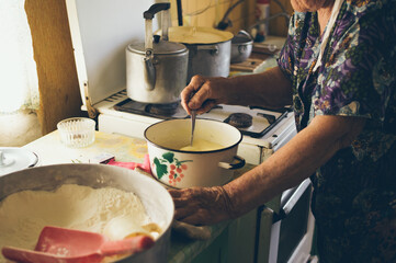 Old grandmother kneads dough for pancakes  in saucepan