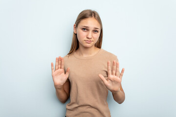 Young caucasian girl isolated on blue background rejecting someone showing a gesture of disgust.