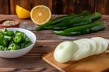 Green hot chili pepper and cut onion on cutting board with lemon on wooden background