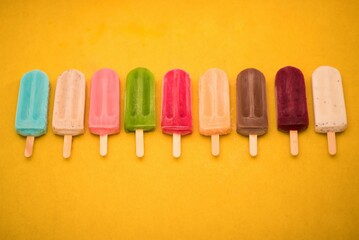 Top view of colorful ice cream bars in row on the yellow background, giving summer vibes