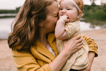 Mom snuggles baby red head daughter on lakeside beach