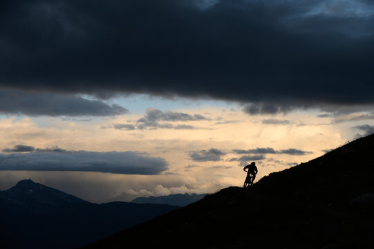 Mountain Biker Cornering on Ridgeline in Loomy Alpine Vista