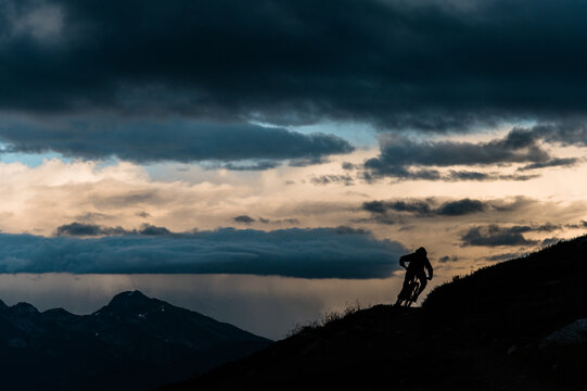 Mountain Biker Cornering on Ridgeline in Loomy Alpine Vista