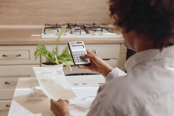 A man , a view from the back, checks the bills on a calculator