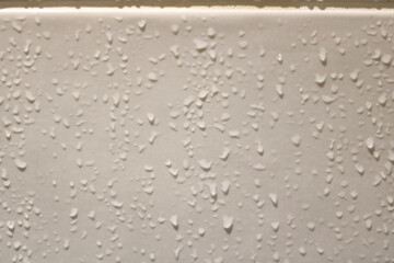 Small water droplets running down wet beige ceramic bathroom tiles