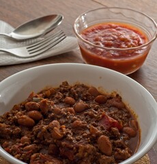 Close-up bowl of chili con carne with salsa bowl flatware napkin in background