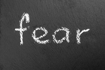 Grunge word FEAR written in chalk on a black rough slate chalkboard