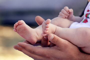 The father holds the baby's pink legs in his hands