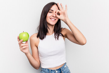 Young caucasian woman holding an apple isolated on white background excited keeping ok gesture on...