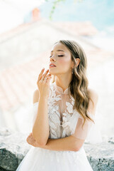 Bride in a white dress touches her chin with her fingers. Portrait