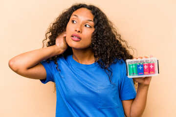 Young hispanic woman holding a recyclable batteries isolated on beige background trying to listening a gossip.