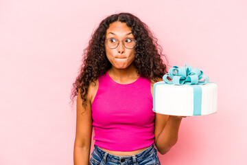 Young caucasian woman holding a cake isolated on pink background confused, feels doubtful and unsure.