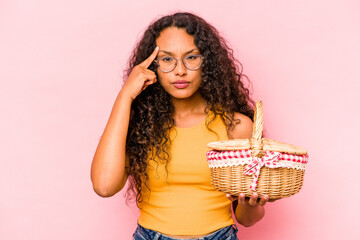 Young hispanic woman doing a picnic isolated on beige background pointing temple with finger, thinking, focused on a task.