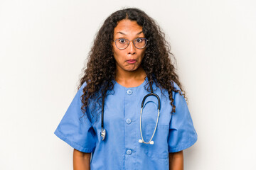 Young hispanic nurse woman isolated on white background shrugs shoulders and open eyes confused.