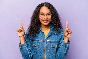 Young hispanic woman isolated on purple background indicates with both fore fingers up showing a...