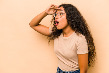 Young hispanic woman isolated on beige background looking far away keeping hand on forehead.