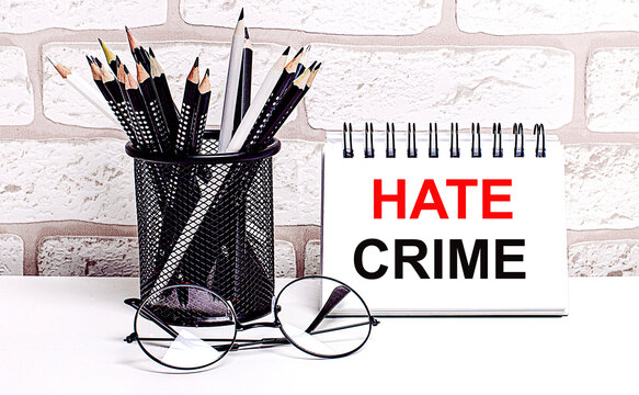 A Workplace In The House With Glasses, Pencils In A Stand And A Notebook With Text HATE CRIME On A Brick Wall Background. Home Office. Scandinavian Style