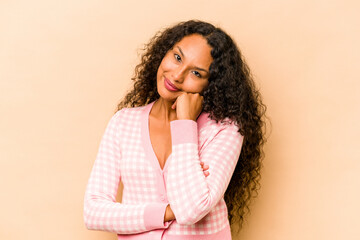 Young hispanic woman isolated on beige background smiling happy and confident, touching chin with hand.