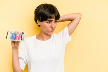 Young caucasian woman holding a batteries box isolated on yellow background touching back of head, thinking and making a choice.