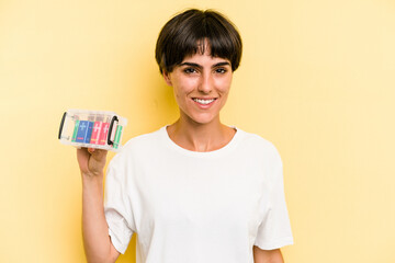 Young caucasian woman holding a batteries box isolated on yellow background happy, smiling and cheerful.